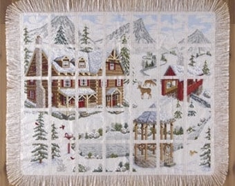 May include: A cross-stitch pattern featuring a snowy winter scene with a cabin, a bridge, and a deer. The pattern is framed with a white fringe.