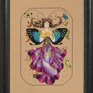 Puede incluir: Obra de arte en punto de cruz enmarcada que representa a una mujer con alas de mariposa y un vestido morado. La mujer sostiene flores, rodeada de mariposas de colores. La obra está en un marco negro, sobre un fondo beige.