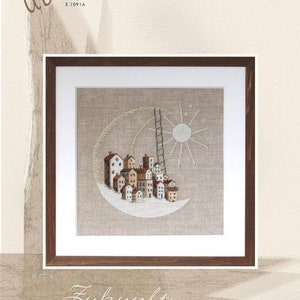 May include: Framed cross-stitch art featuring a whimsical village scene. The artwork depicts a crescent moon with a ladder leading to a sun and stars. The houses are in shades of brown and white. The frame is a dark wood.