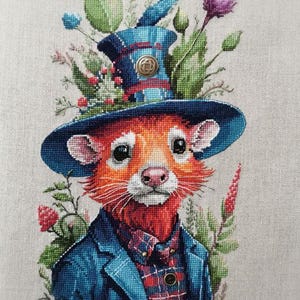 May include: Cross-stitch portrait of a rodent wearing a blue hat with floral accents and a matching blue blazer over a plaid shirt. The rodent has orange fur, a pink nose, and a red beard. The artwork is detailed and colorful.