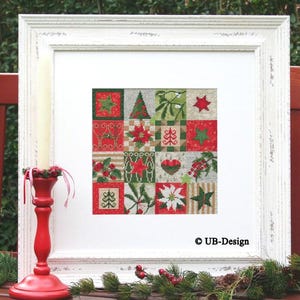 May include: A white frame with a red and green Christmas-themed cross-stitch design. The design features a variety of holiday symbols, including stars, trees, poinsettias, and holly. The frame is sitting on a table with a red candle holder and green foliage.