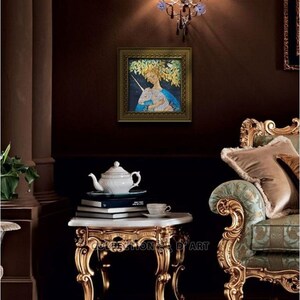 May include: A framed artwork depicts a woman with a unicorn, set against a backdrop of foliage. The artwork is displayed in a room with ornate furniture, including a gold-trimmed side table with a white teapot and books. The room has a dark brown wall.