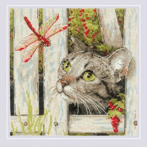 May include: Cross-stitch artwork featuring a gray tabby cat peeking through a white picket fence. A red and pink dragonfly hovers near the fence. Green foliage and red berries add color to the scene.