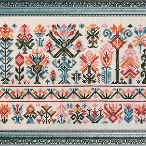 May include: A framed cross-stitch sampler with a floral design. The embroidery features a variety of colourful flowers and geometric patterns in shades of orange, pink, blue, and green. The frame is a muted teal colour.