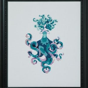 May include: Cross-stitch art of a teal and blue octopus-like figure with a woman's upper body and flowing teal hair. The figure is framed in a black square frame, set against a white background. The octopus's tentacles are detailed with pink accents.