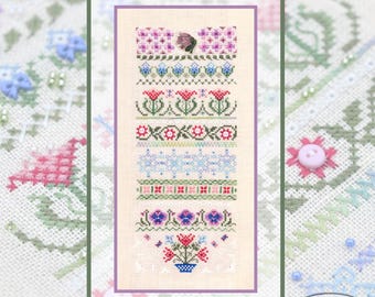 May include: A cross-stitch sampler featuring various floral and geometric patterns in shades of pink, blue, green, and red. The sampler is framed with a green border and a purple inner border. The Tela Artis logo is in the bottom right corner.