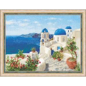May include: Framed cross-stitch art depicting a coastal scene with white buildings, blue domes, and a vibrant blue sea. Red flowers in terracotta pots add a pop of color. The artwork is set against a light blue sky.