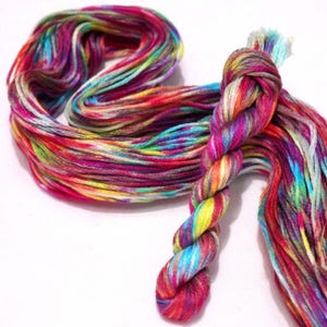 May include: A skein of embroidery floss featuring a vibrant, multi-colored variegated pattern. The thread displays a blend of bright pink, yellow, blue, purple, and orange hues, twisted into a long, continuous strand with a knotted section.