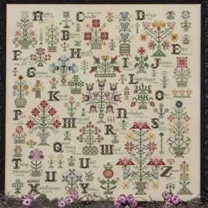 May include: A framed cross-stitch sampler featuring floral and alphabet designs in various colors. The sampler includes letters A through Z, with each letter accompanied by a unique floral motif. The background is a light beige color.