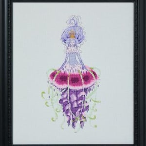 May include: Cross-stitch art of a jellyfish in a black frame. The jellyfish features a lavender head, a magenta and purple body, and green tendrils. The artwork is detailed and colorful, showcasing a unique marine theme.