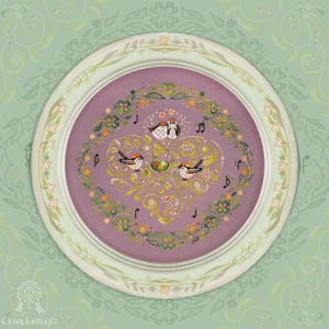 Könnte beinhalten: Gerahmte Kreuzstich-Stickerei mit Vögeln und Noten. Das Design befindet sich auf einem lavendelfarbenen Hintergrund in einem weißen, runden Rahmen. Die Stickerei enthält Blumen- und Blattmotive, mit dem Owl Forest-Logo unten.
