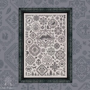 May include: Framed cross-stitch sampler with nature-themed motifs in grey and white. The design includes birds, trees, deer, and geometric patterns. The frame is dark green and the background is a grey pattern.