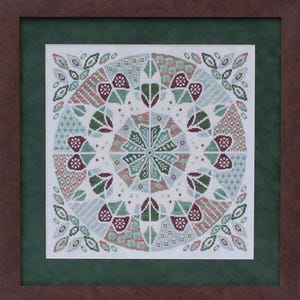Puede incluir: Obra de arte en punto de cruz enmarcada con un diseño circular simétrico. El diseño incorpora formas geométricas y motivos florales en tonos verdes, rojos y verde azulado sobre un fondo blanco. El marco es marrón con un paspartú verde.