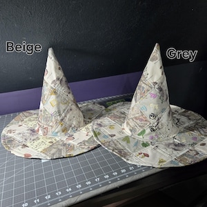 May include: Two witch hats with wide brims and pointed tops. The hats are made of quilted fabric with a patchwork design featuring stamps, letters, and other vintage elements. One hat is labeled "Beige" and the other "Grey".