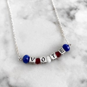 May include: A silver chain necklace with a red, white, and blue beaded charm that spells out "VOTE".