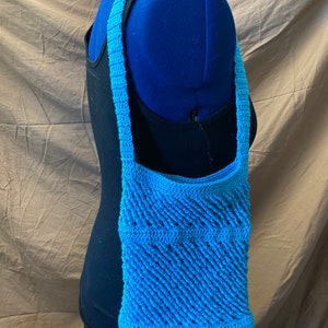 以下が含まれることがあります： シンプルな幾何学模様の明るいブルーのクロシェショルダーバッグです。