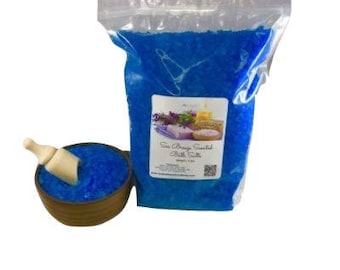 Może przedstawiać: Torebka z niebieskimi solami do kąpieli i chochla z solami w drewnianej misce. Torebka ma etykietę z napisem "Sea Breeze Scented Bath Salts".