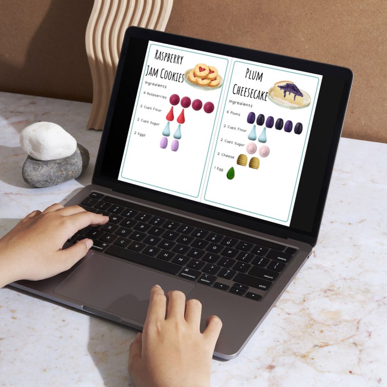 May include: A laptop computer open to a recipe page with two different recipes for Raspberry Jam Cookies and Plum Cheesecake. The recipes are illustrated with colorful icons and ingredients listed.