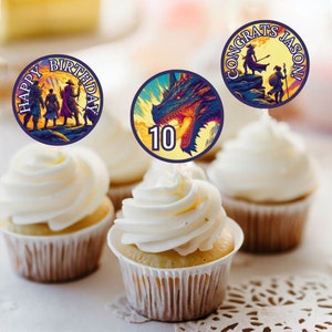 以下が含まれることがあります： ファンタジーをテーマにした丸いカップケーキトッパーが3つ。1つのトッパーには10の数字が書かれたドラゴンが描かれ、もう1つは「ハッピーバースデー」と冒険者グループが描かれ、最後の1つは「おめでとうジェイソン！」と2人の冒険者が描かれています。
