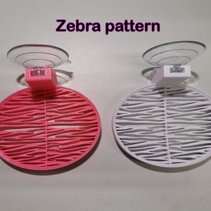 May include: Two suction cup holders with a zebra pattern. One is pink and the other is white.