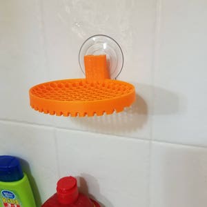 May include: Orange plastic shower caddy with a suction cup mount. The caddy has a honeycomb design and is attached to a white tiled wall.