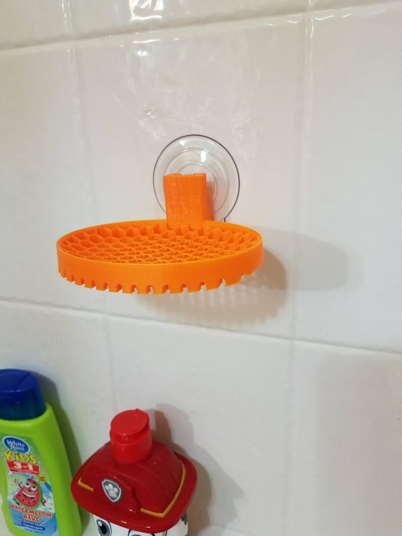 May include: Orange plastic shower caddy with a suction cup mount. The caddy has a honeycomb design and is attached to a white tiled wall.