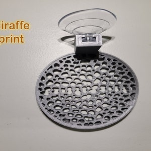 May include: A gray 3D printed suction cup holder with a circular, patterned design. The text "Giraffe print" is visible in the image.