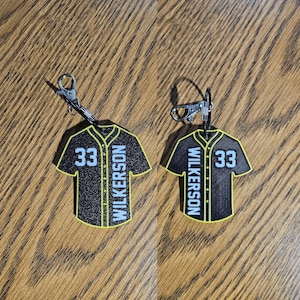Peut inclure: Deux porte-clés en forme de maillot de baseball noir et jaune avec le numéro 33 et le nom "WILKERSON" imprimé dessus.