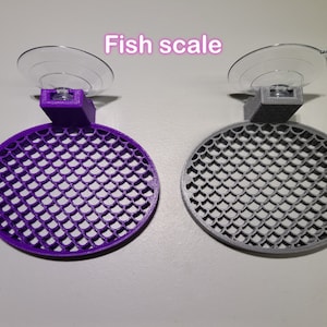 May include: Two fish scale-shaped suction cup holders, one purple and one gray. The holders are designed to attach to a smooth surface, such as a glass aquarium.