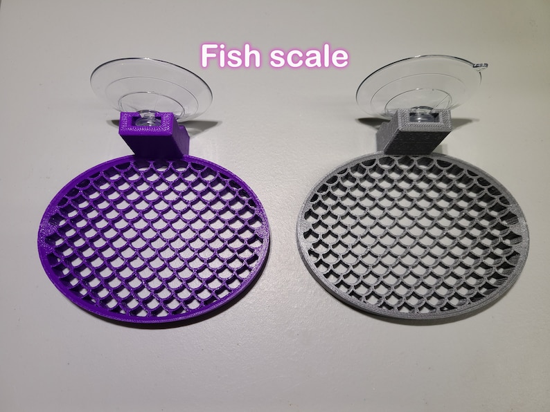 May include: Two fish scale-shaped suction cup holders, one purple and one gray. The holders are designed to attach to a smooth surface, such as a glass aquarium.