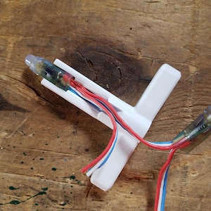 May include: A white plastic T-shaped connector with three wires running through it. The wires are red, white, and blue. The connector is used to connect LED lights.