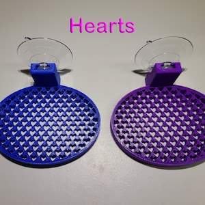 May include: Two suction cup wall mounts with a heart-shaped design. The mount on the left is blue and the mount on the right is purple.