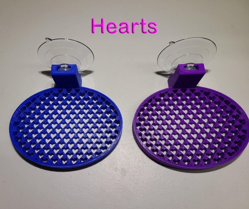 May include: Two suction cup wall mounts with a heart-shaped design. The mount on the left is blue and the mount on the right is purple.