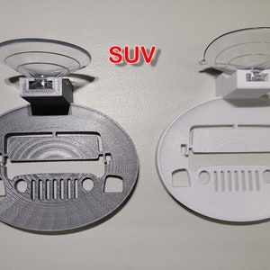 May include: Two 3D printed car-shaped suction cup holders. One is gray and the other is white. Both have a cutout of a Jeep SUV and a suction cup on top. The word "SUV" is printed in red on the image.