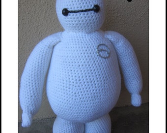 May include: White crocheted Baymax plush toy from the Disney movie Big Hero 6. The toy has a black eye design and a silver circle on its chest.