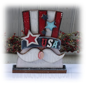 May include: A wooden Uncle Sam figurine with a red, white, and blue top hat, stars, and a mustache. The word "USA" is displayed on a banner. The patriotic decoration is perfect for Independence Day.