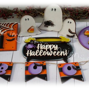 May include: A set of Halloween decorations featuring a black cauldron with the text "Happy Halloween!" in white, a purple sign with the text "Trick or Treat" in gold, a banner with the letters "BOO" in purple, a sign with the number "31" on an orange background, and three white ghosts with black eyes.
