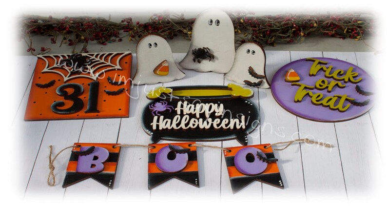 May include: A set of Halloween decorations featuring a black cauldron with the text "Happy Halloween!" in white, a purple sign with the text "Trick or Treat" in gold, a banner with the letters "BOO" in purple, a sign with the number "31" on an orange background, and three white ghosts with black eyes.