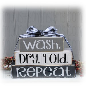 May include: Stacked wooden blocks with the words "Wash, Dry, Fold, Repeat" in black and white lettering. The blocks are decorated with a black and white checkered ribbon.