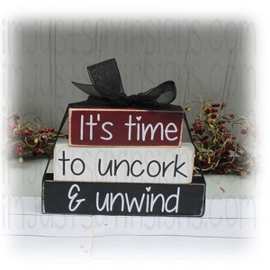 May include: Three wooden blocks stacked on top of each other. The top block is red and says "It's time". The middle block is white and says "to uncork". The bottom block is black and says "& unwind".