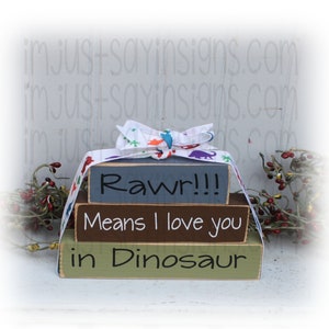 May include: Three wooden blocks stacked on top of each other. The top block is painted blue and says "Rawr!!". The middle block is painted brown and says "Means I love you". The bottom block is painted green and says "in Dinosaur".