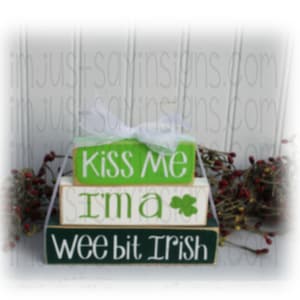 May include: Three wooden blocks stacked on top of each other. The top block is green and says "Kiss Me". The middle block is white and says "I'm a" with a green shamrock. The bottom block is green and says "Wee Bit Irish".