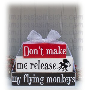 May include: Three wooden blocks stacked on top of each other. The top block is red and says "Don't make". The middle block is white and says "me release". The bottom block is black and says "my flying monkeys". A black and white silhouette of a monkey with wings is on the middle block.