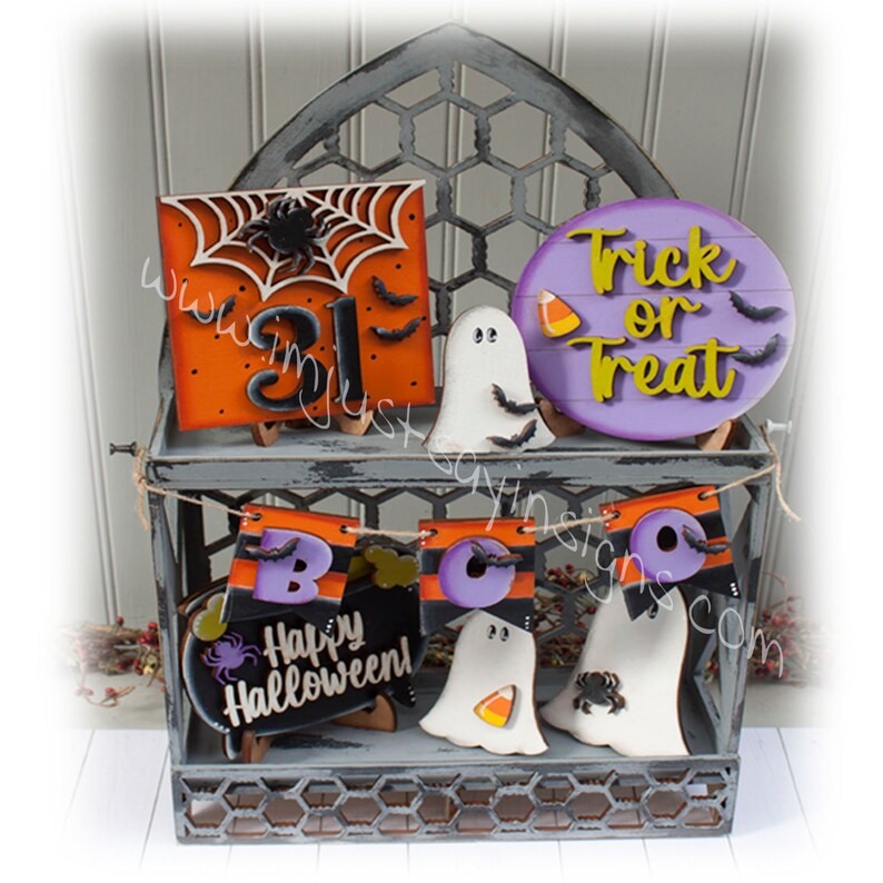 May include: A set of Halloween-themed wooden signs with various designs, including a ghost, a spider web, a banner that says "BOO", and a sign that says "Happy Halloween!" The signs are displayed on a wire shelf with a gray background.