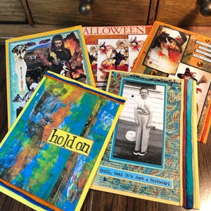 Puede incluir: Una colecci&oacute;n de tarjetas de arte hechas a mano con varios dise&ntilde;os. Una tarjeta presenta el texto "hold on" sobre un fondo abstracto colorido. Otras tarjetas tienen im&aacute;genes y texto vintage, incluyendo un tema de Halloween y una foto en blanco y negro.