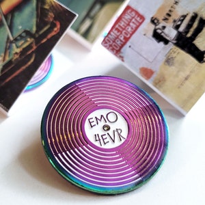 May include: A rainbow iridescent enamel pin shaped like a vinyl record with the text "EMO 4EVR" in white on the center label.