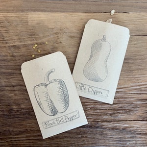 May include: Two brown paper seed packets with black ink drawings of vegetables. The first packet shows a black bell pepper and says "Black Bell Pepper". The second packet shows a squash and says "Little Dipper".