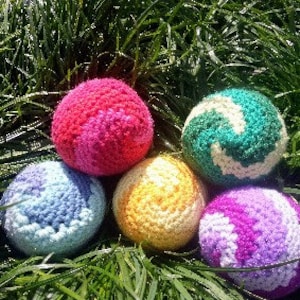 Può includere: Cinque palle all'uncinetto in diversi colori e motivi. Le palle sono rosa e bianca, verde e bianca, azzurro e bianca, gialla e viola e bianca.