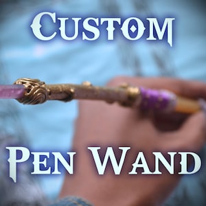 Op de afbeelding: Een aangepaste pen-toverstaf met een paarse kristallen punt, gouden accenten en een paarse en gouden omwikkelde handvat. De toverstaf wordt in een hand gehouden, met het woord "CUSTOM" in blauwe letters boven de toverstaf en de woorden "PEN WAND" in blauwe letters onder de toverstaf.
