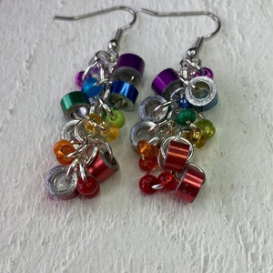 May include: A pair of handmade dangle earrings with silver-tone hooks. Each earring features a cluster of colorful metal rings in red, orange, yellow, green, blue, and purple, along with small, round, colorful beads.